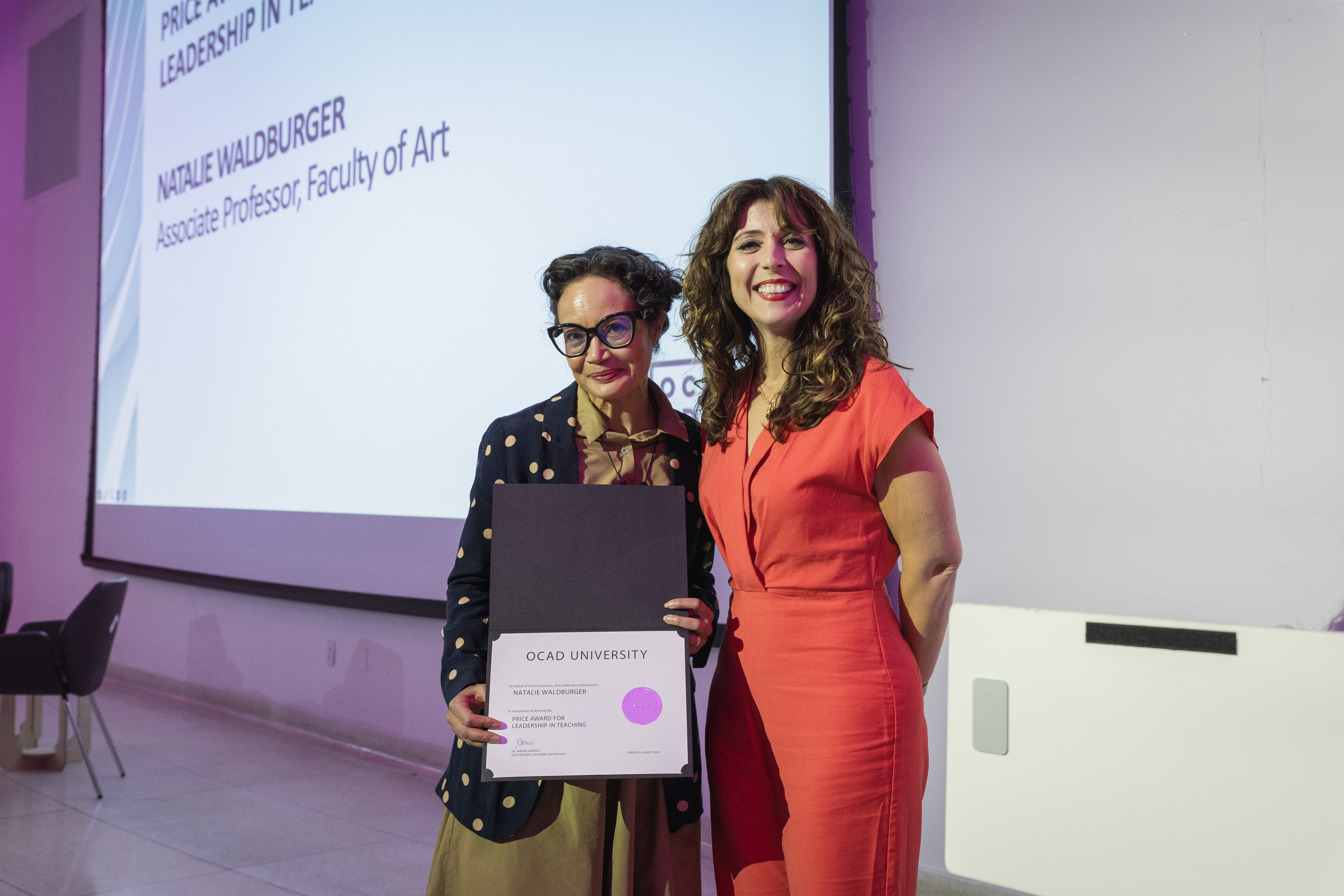 Left to right: Natalie Waldburger and Dr. Gabriele, standing in front of a white screen. 