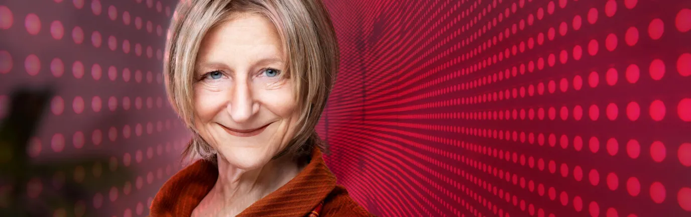 Photo of a woman with medium length blond hair with background of red computer-like squares