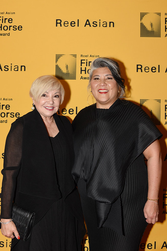 Two women standing together in front of a background that says Reel Asian Fire Horse Award.