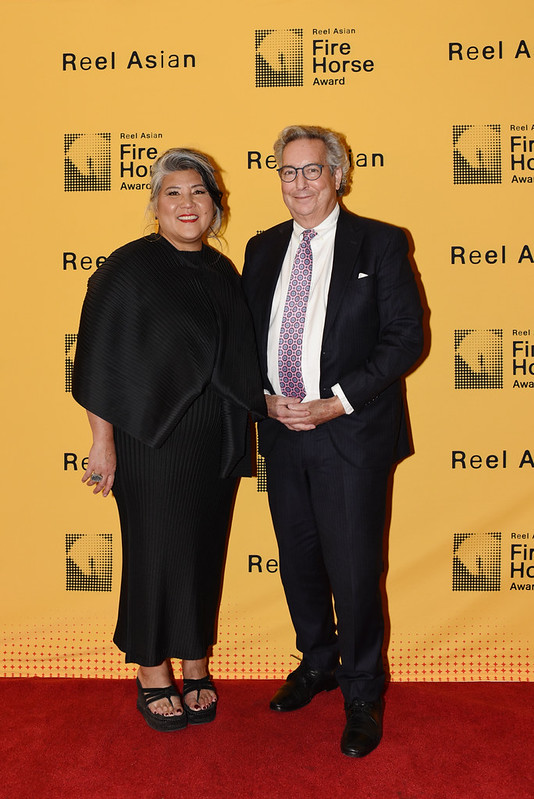 Ana Serrano stands next to Jaime Watt in front of a background that says Reel Asian Fire Horse Award