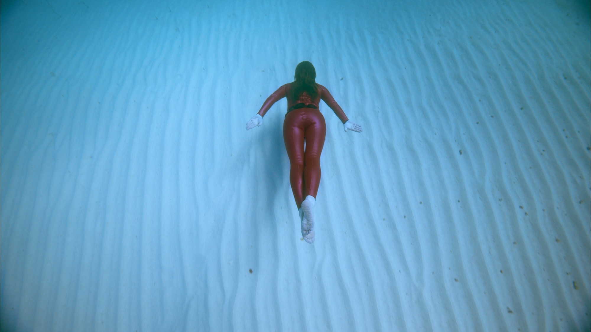A woman in red swimsuit swimming along the bottom of an ocean