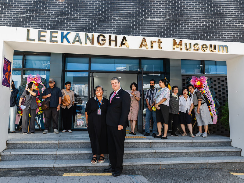 Two peopel standing in front of LeeKangha Art Museum, woman on left, man on right, with people in background