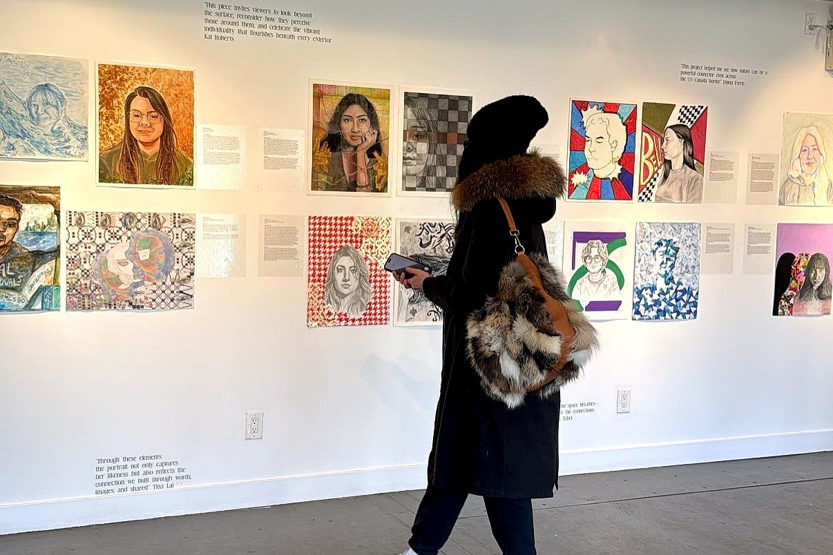 A woman wearing black, lookin at artworks on a wall. 