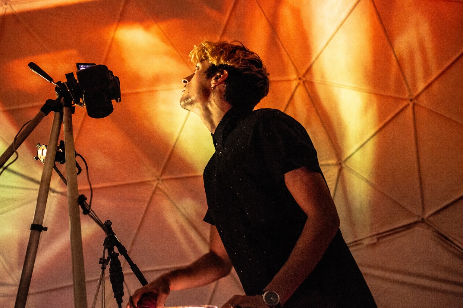 Image of man in front of a man looking upward at a tent bathed in yellow orange light