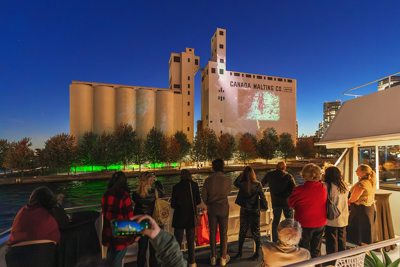 People on a boat look at art projection on Canada Malting Silos.