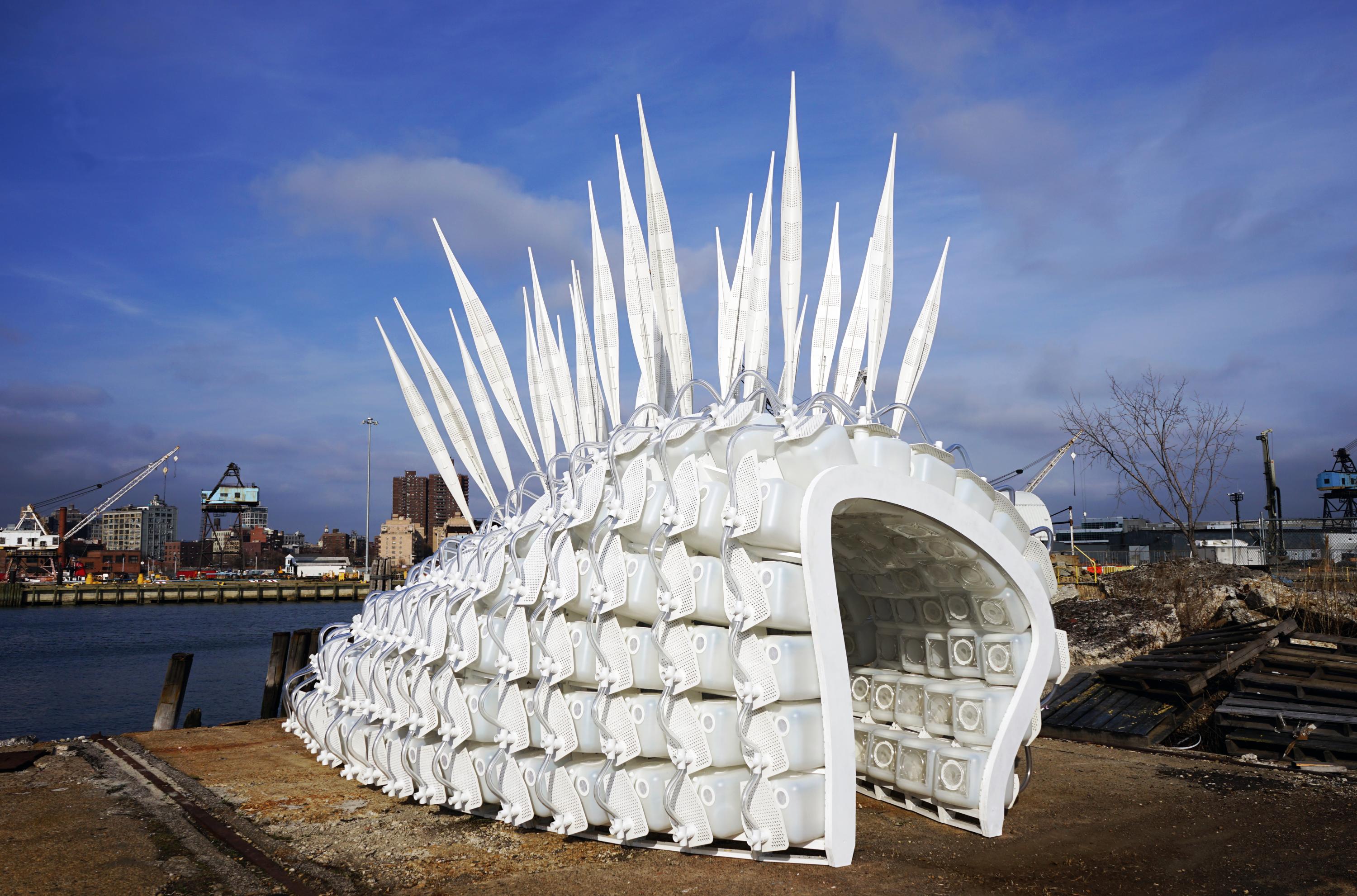 A white modular structure made of insect incubators, photographed outdoors in front of blue sky. 