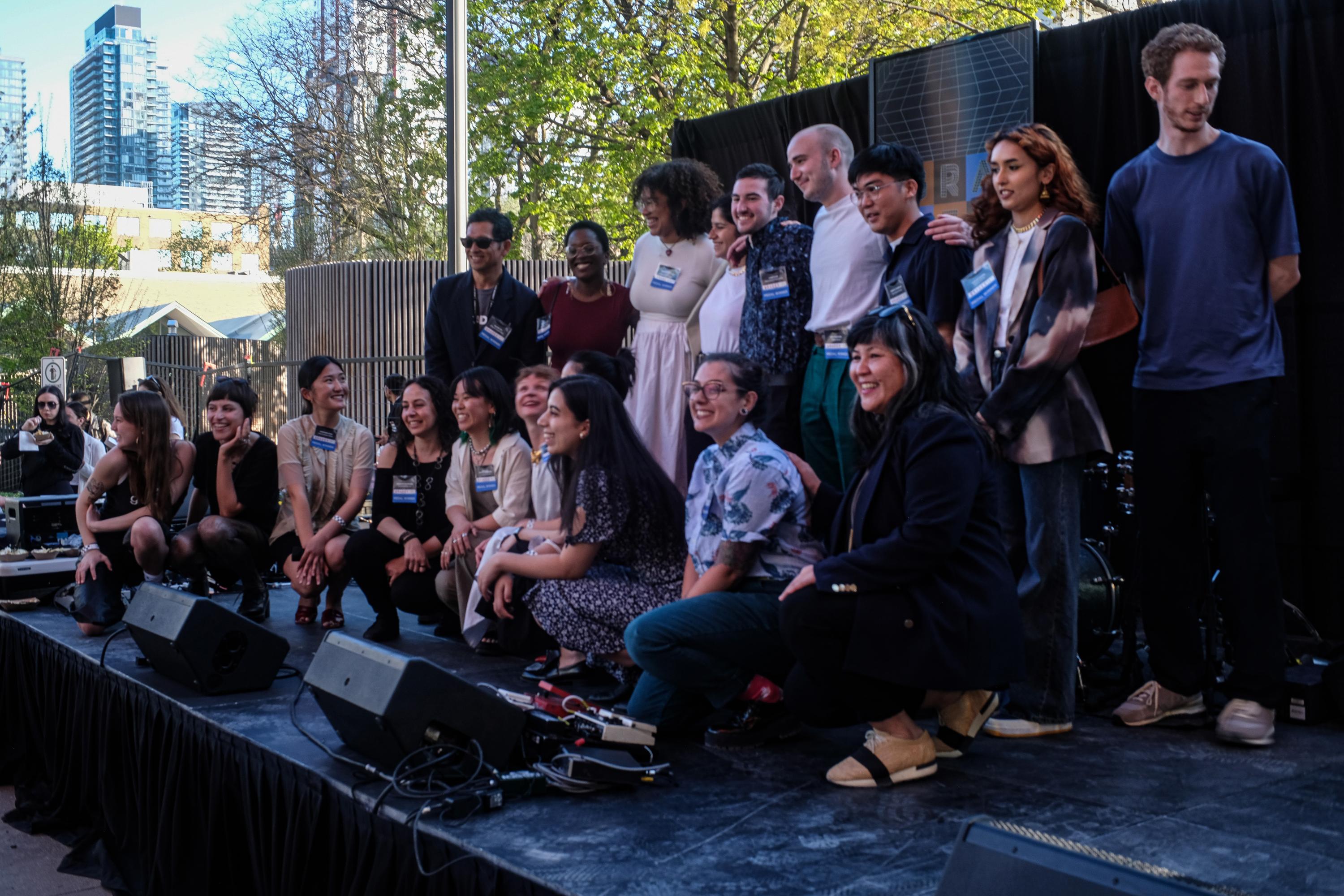 A group of OCAD University graduates standing on stage outside, smiling.