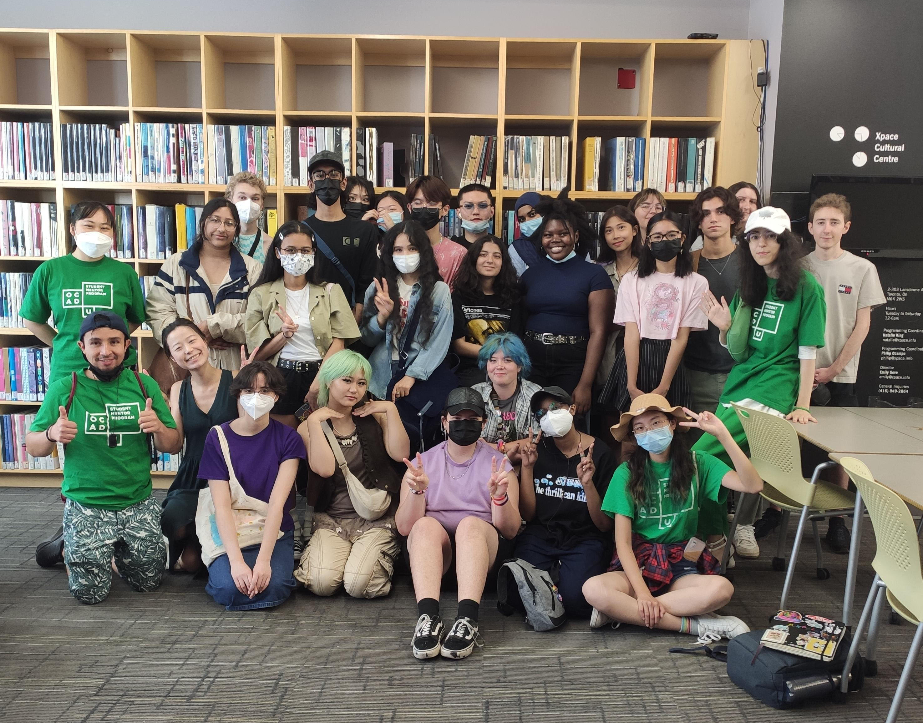 A large group of students pose in front of a book shelf.
