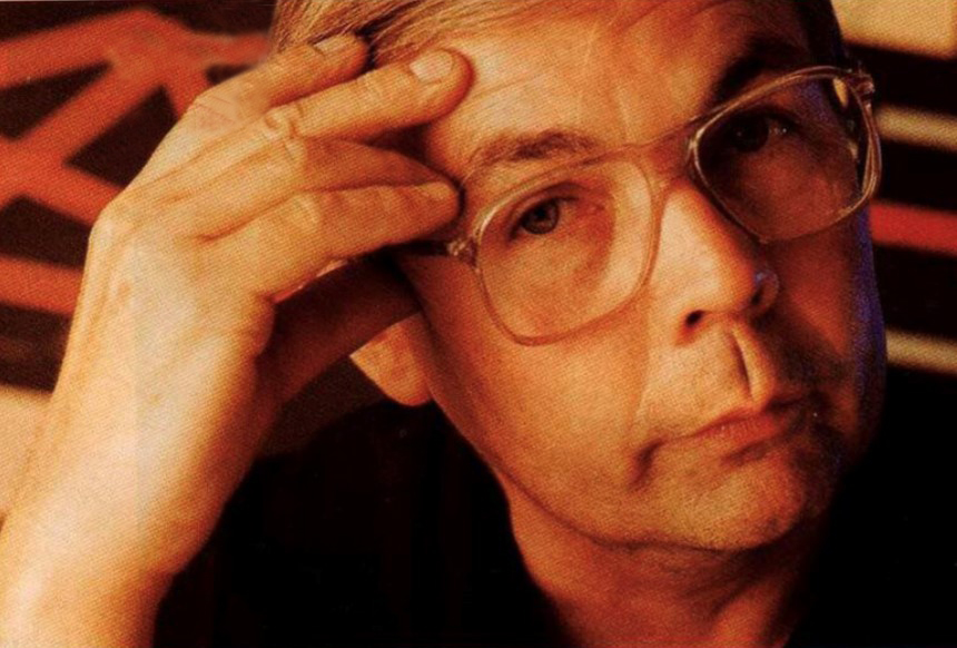 A portrait of Claude Gidman wearing glasses leaning his face on this hand.