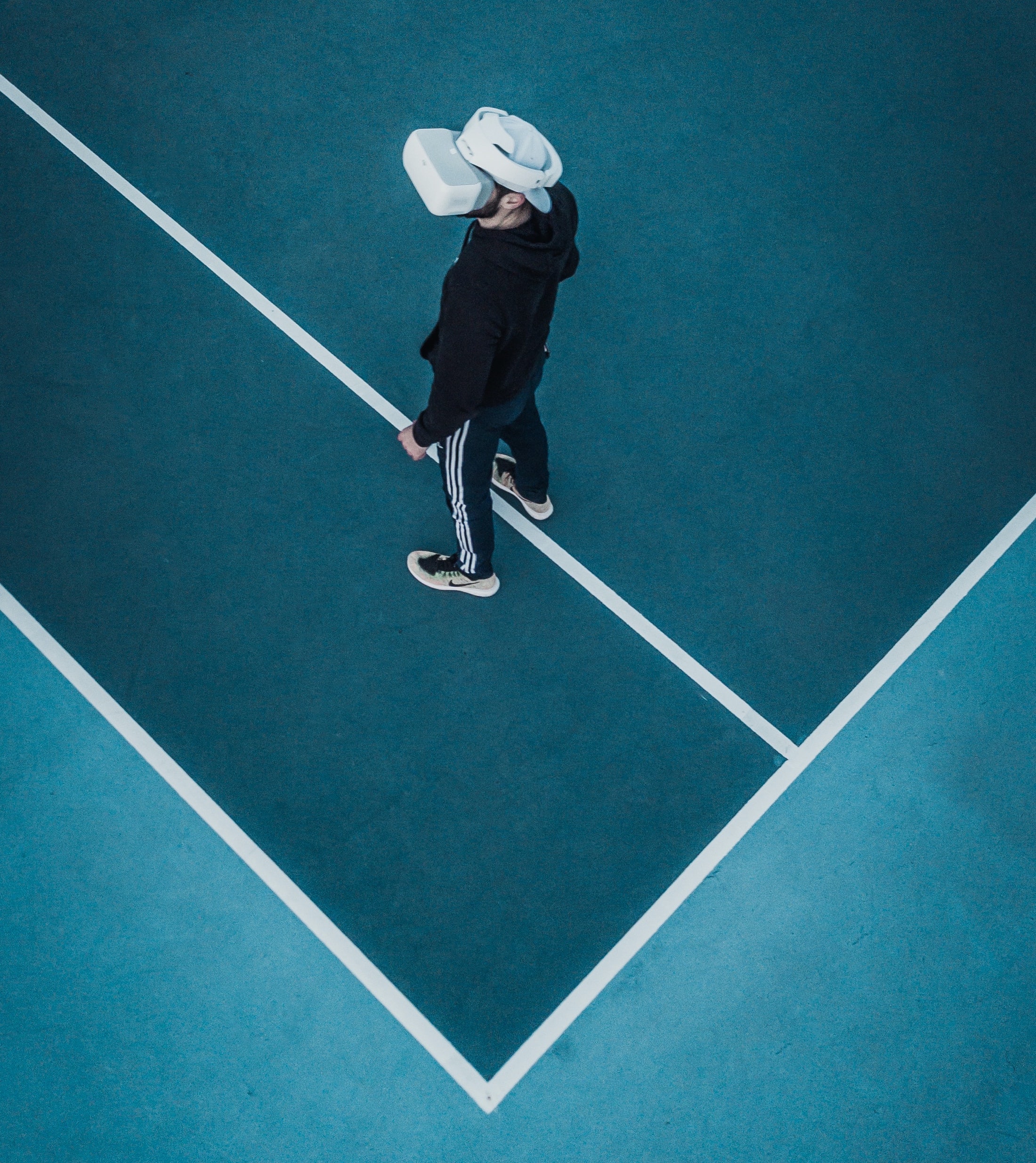 A person standing on a tennis court wearing virtual reality goggles.