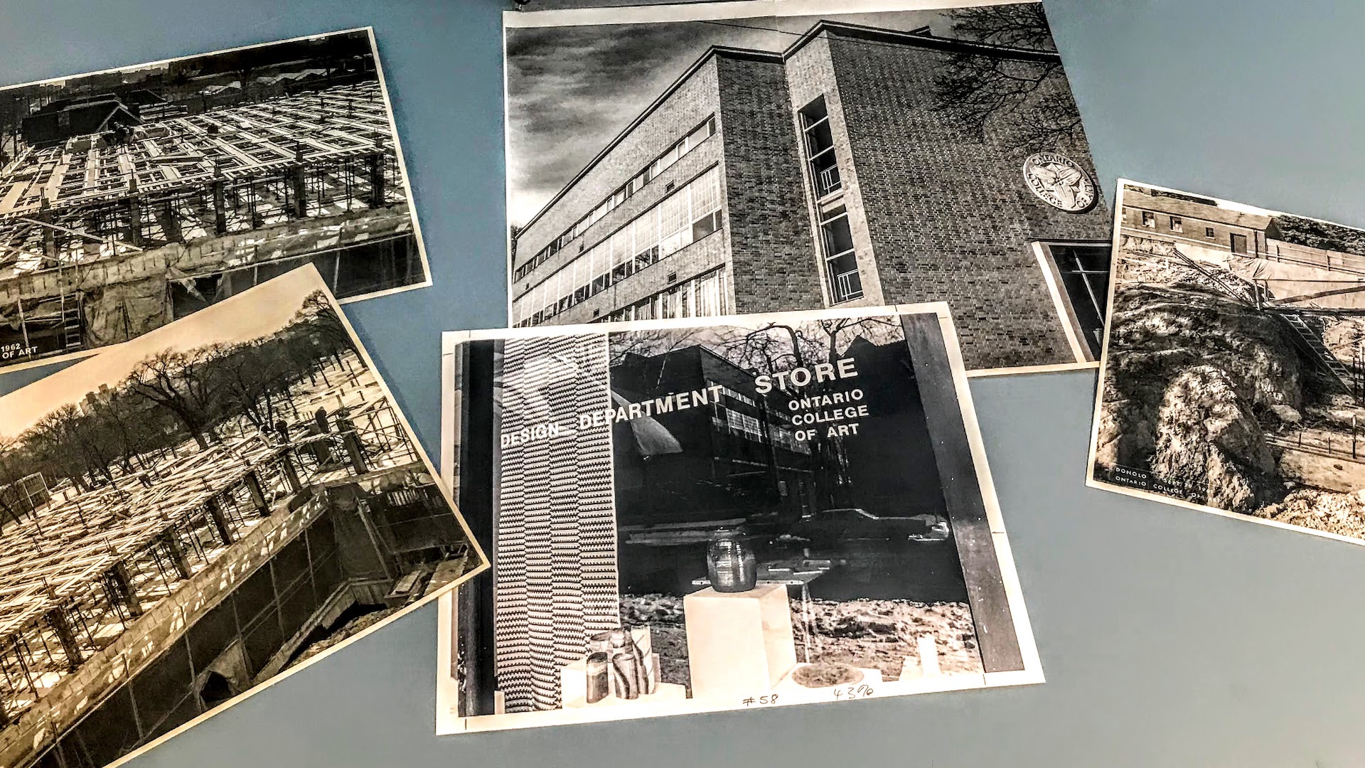 Image consists of archival photographs laid out on a table. The photographs show Ontario College of art buildings, the construction of a new wing at 100 McCaul Street and the Design Department Store for the Ontario College of Art in the 1960’s.