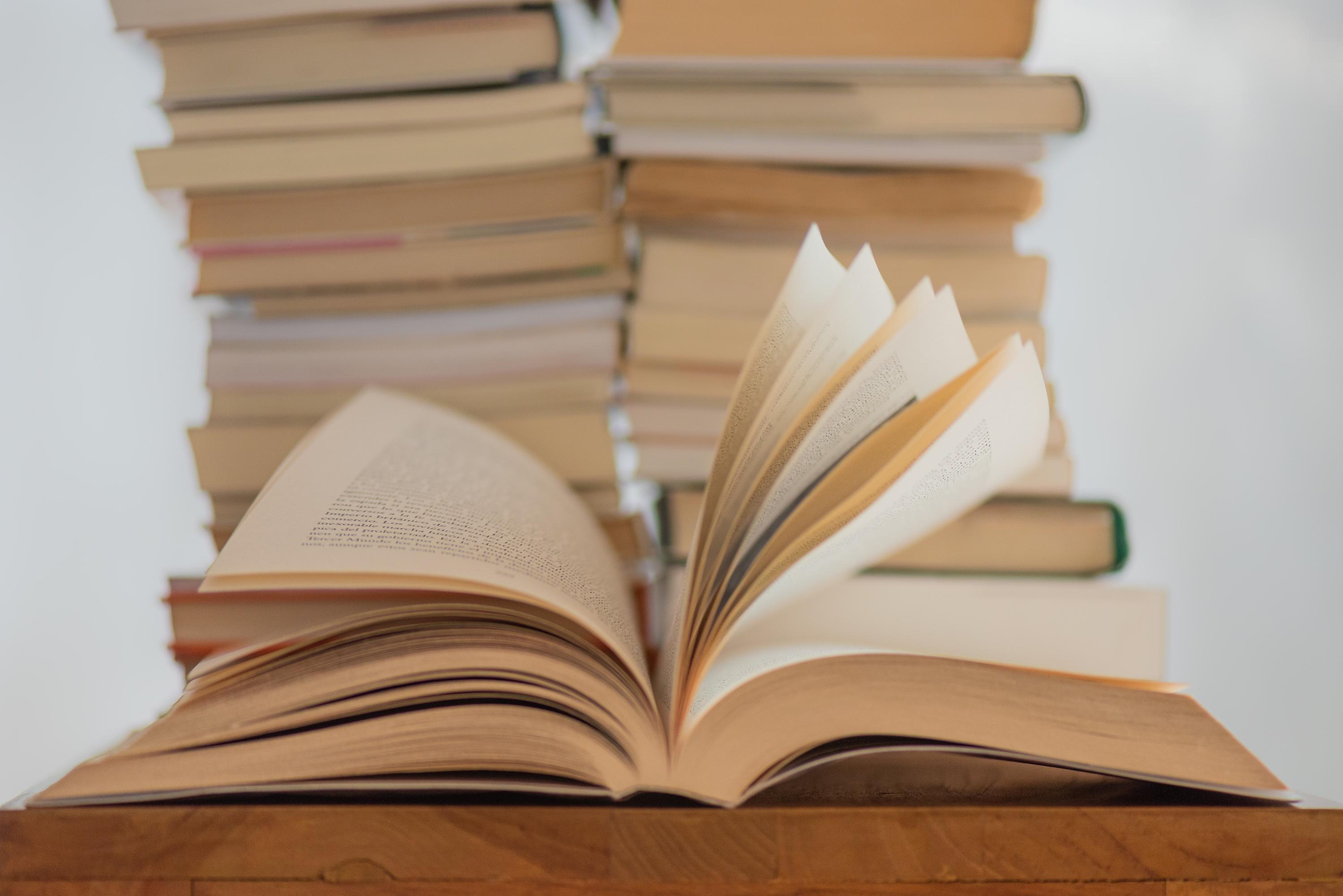 An open book on a desk with two stacks of books in the background.