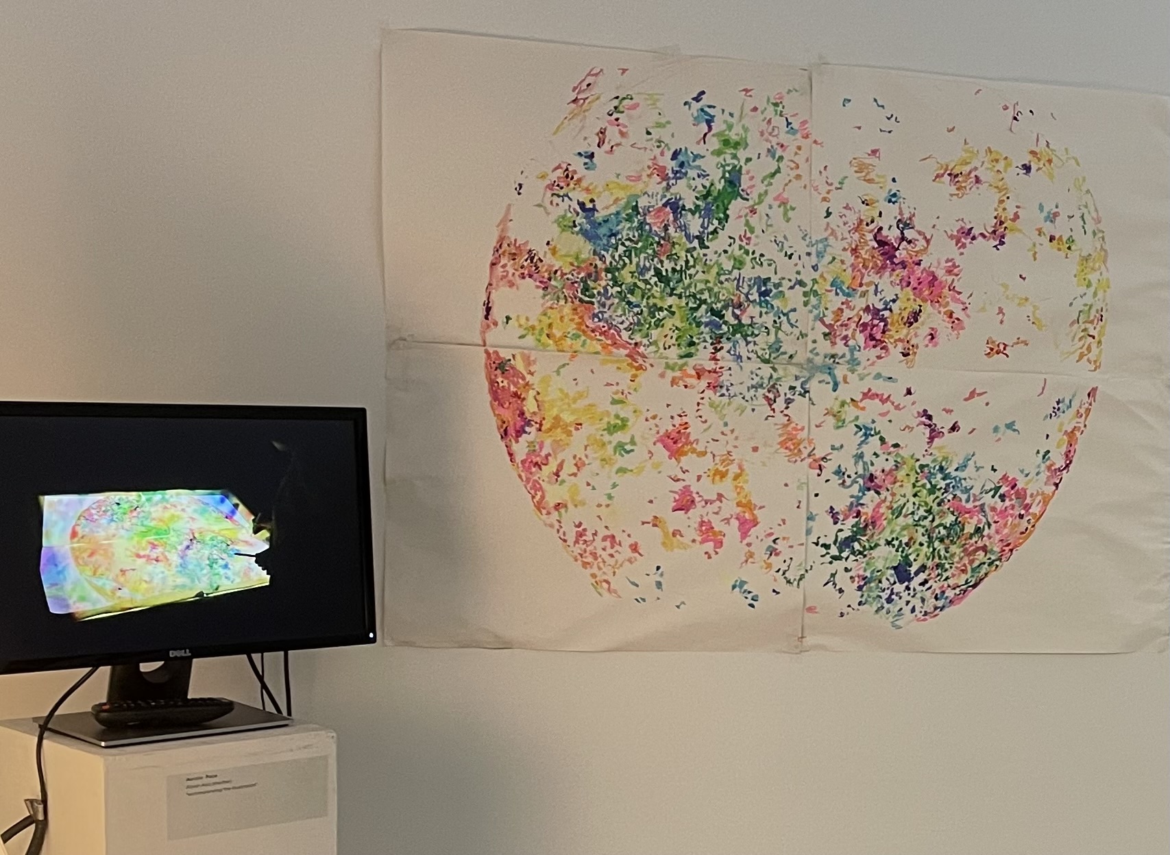 Four sheets join together to create a depiction of the earth in beautiful colourful markings. Also showing is a still from the accompanying video depicting the art work being created
