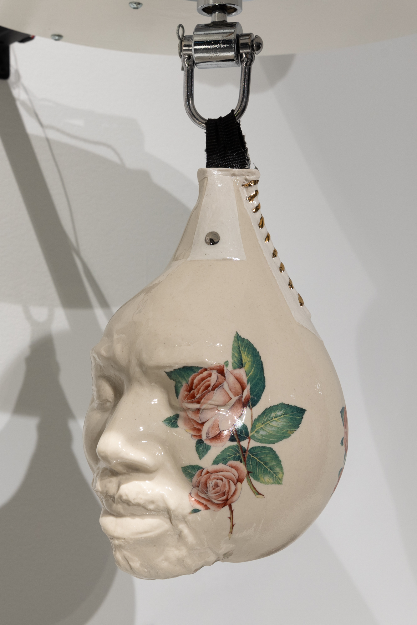 A face embedded on a ceramic punching bag with golden stitching on the side and a rose motif on the right side of the face. 