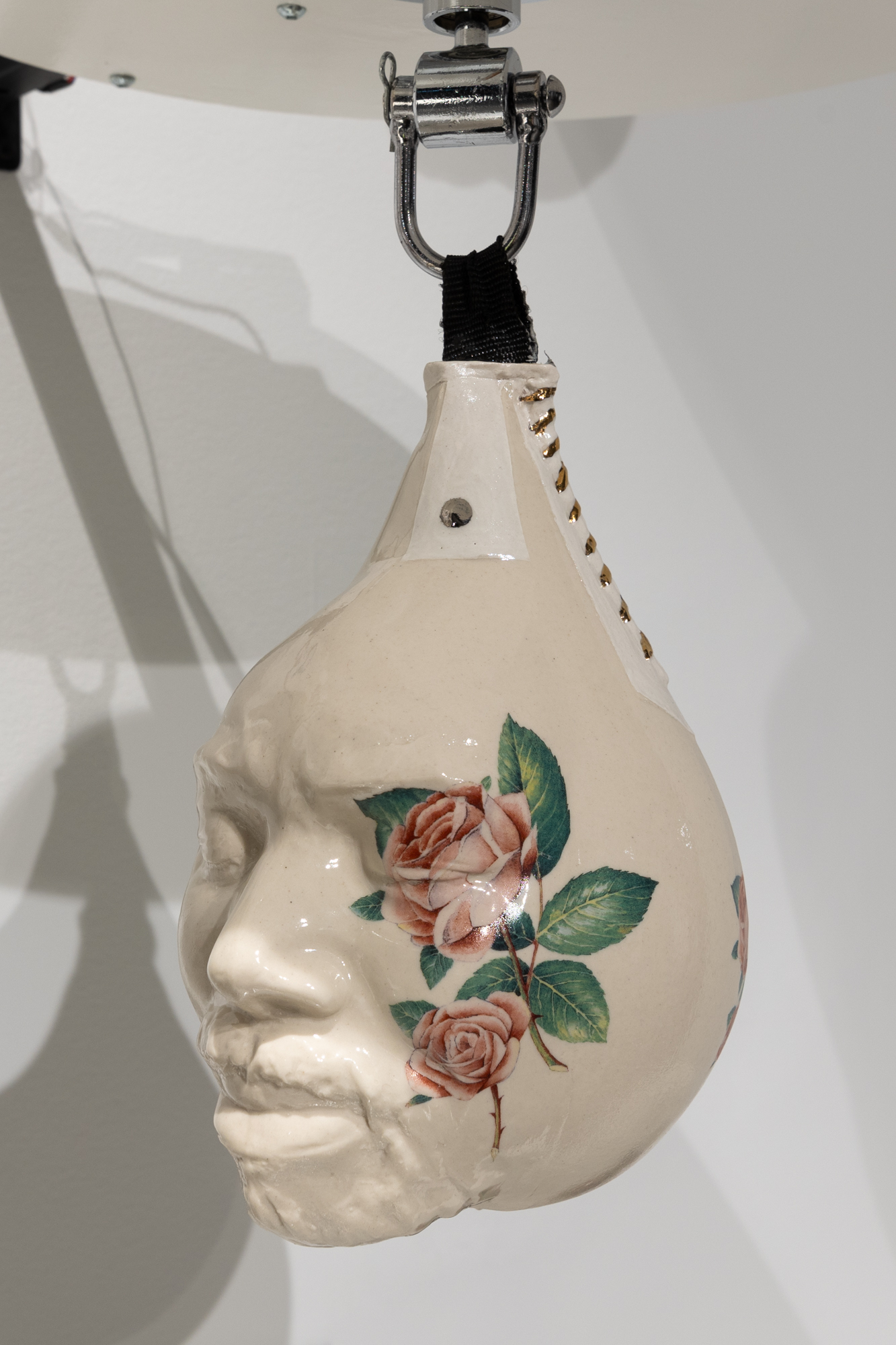 A face embedded on a ceramic punching bag with golden stitching on the side and a rose motif on the right side of the face.