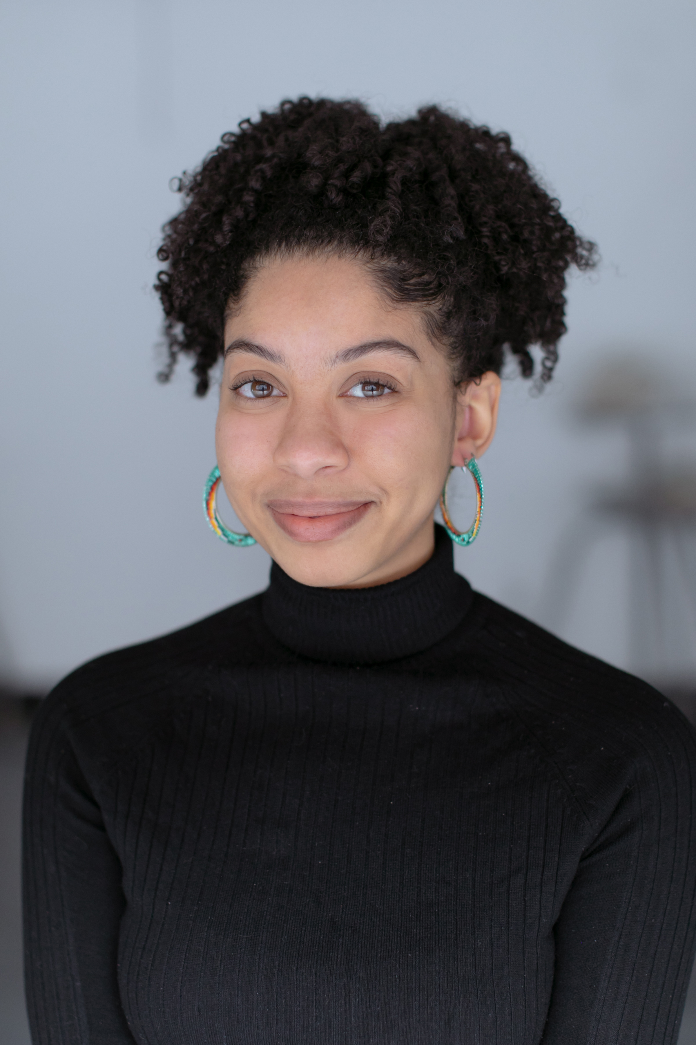 A woman with tied back curly hair smiling and wearing a black turtle neck. 