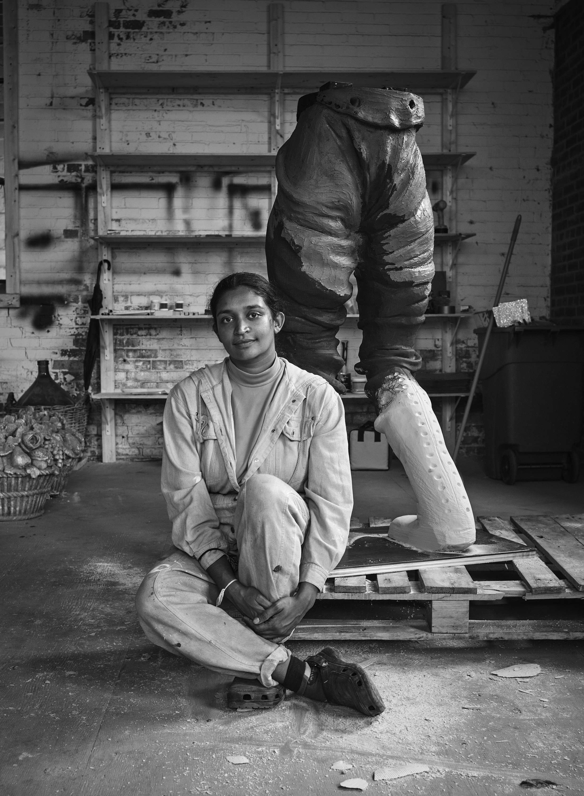 A black and white picture of a full body image of a woman wearing overalls smiling at the camera.