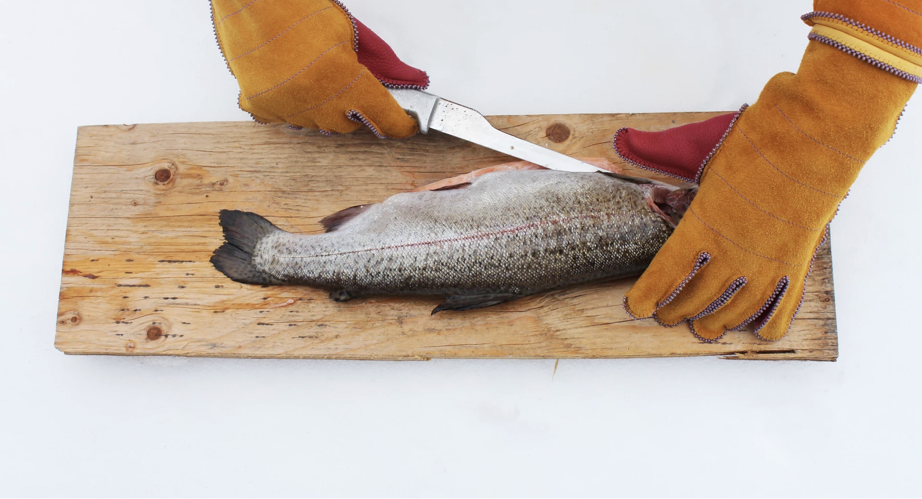 Photograph of yellow-gloved hands filleting a trout on a wooden cutting board.