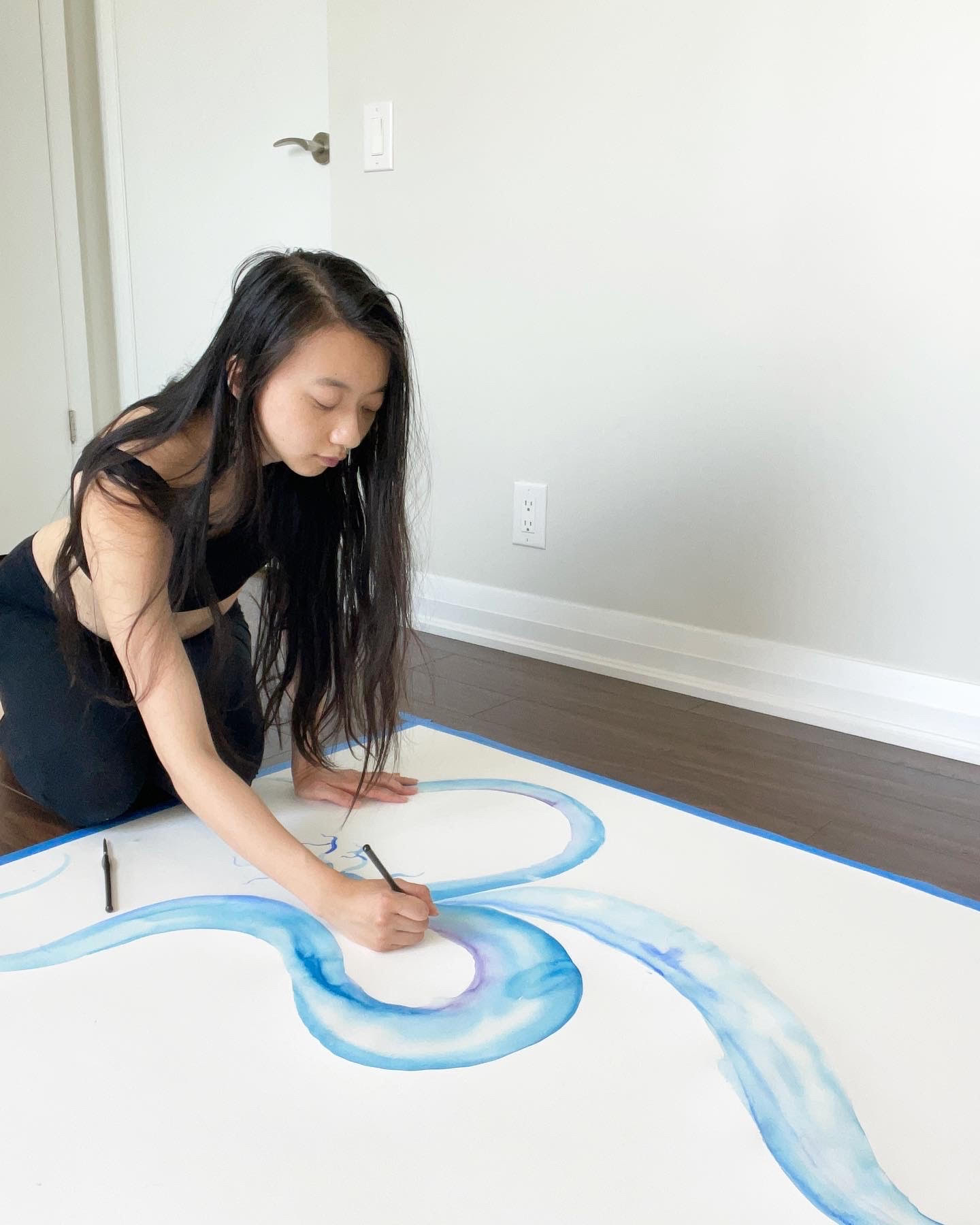 A woman (Jenny) paints in blue watercolour on a canvas on a wooden floor.