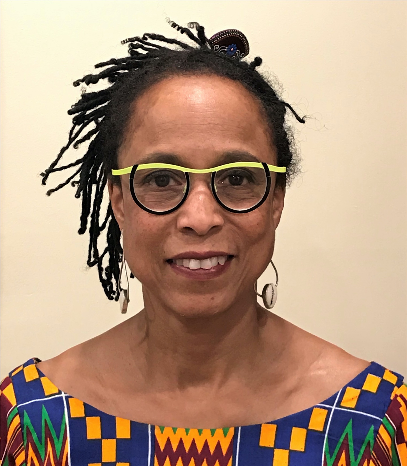 A woman with tied black curly hair, wearing a lime green and black eye glasses smiling at the camera