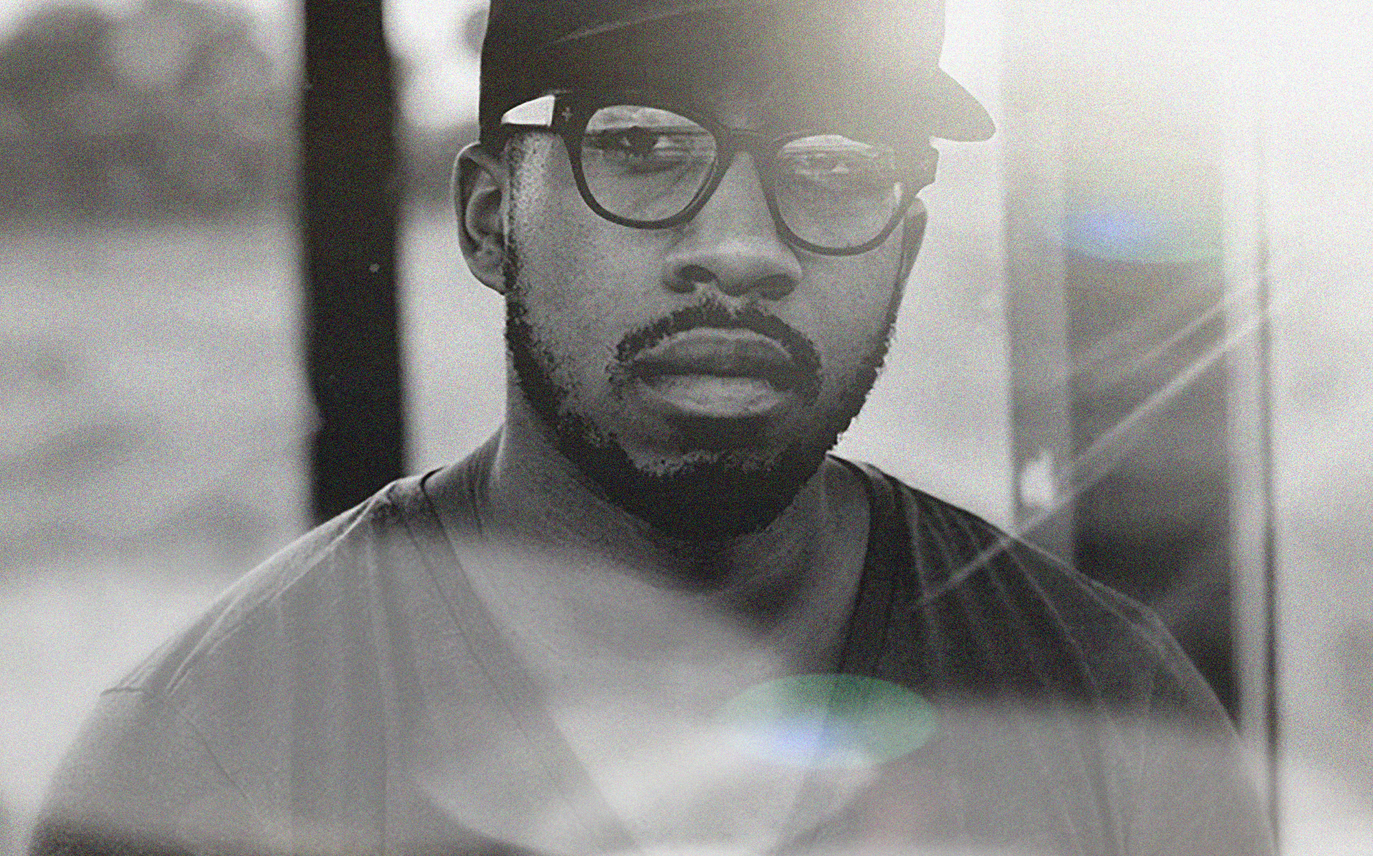 A bearded man wearing a black hat, eye glass and t-shirt in black and white picture