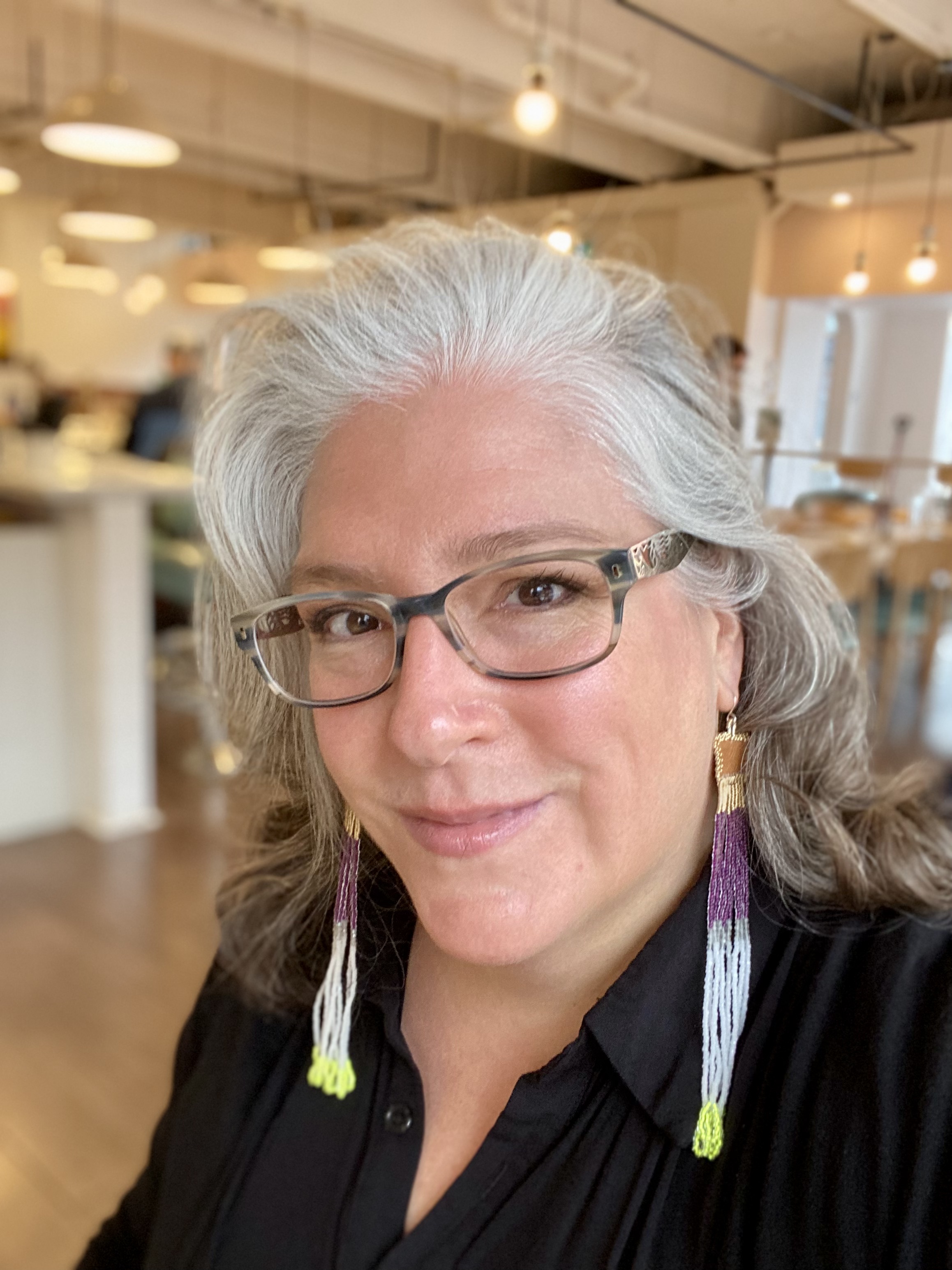 A woman with light grey loose hair at shoulder length wearing long beaded earrings smiling at the camera