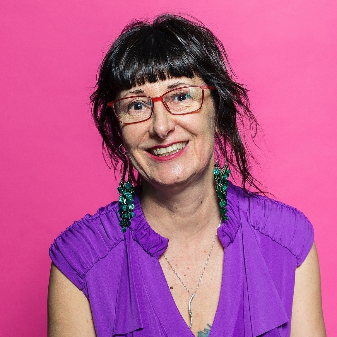 An image of a woman with tied brown hair, smiling wearing eye glasses. 