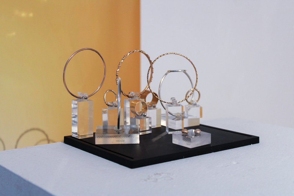 Different sized metal/wire rings mounted on small, translucent platforms, sitting on a black platform, against a yellow and white wall.