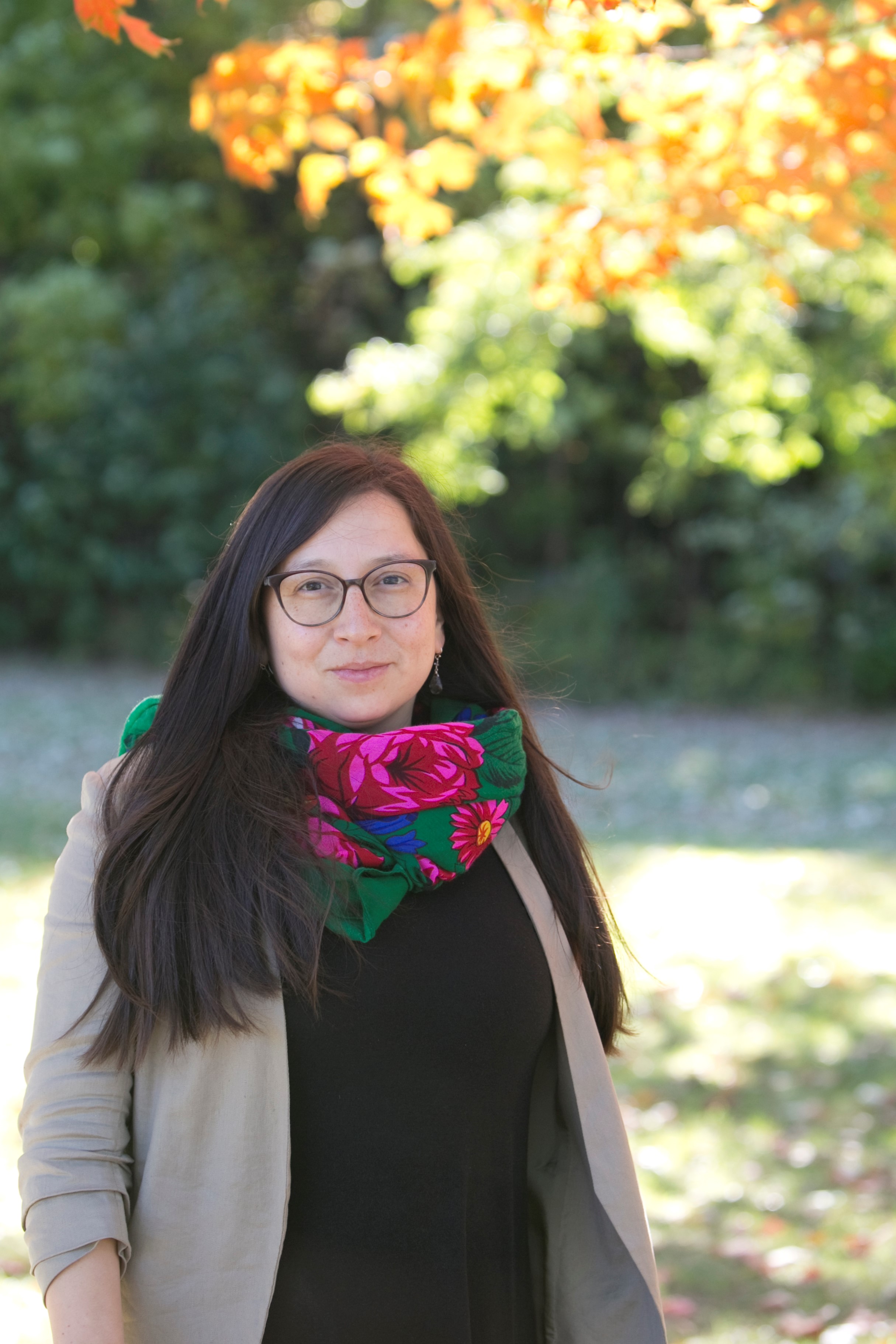 An image of woman with long black hair wearing eye glasses smiling at a camera.