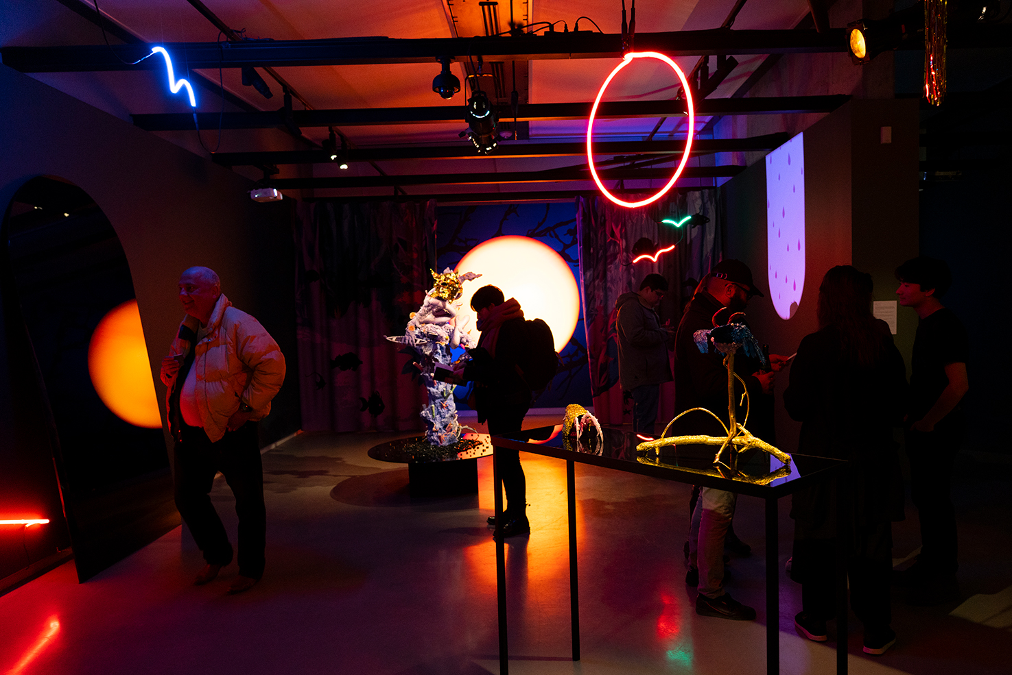 Dark room with people in foreground and works of art, neon light