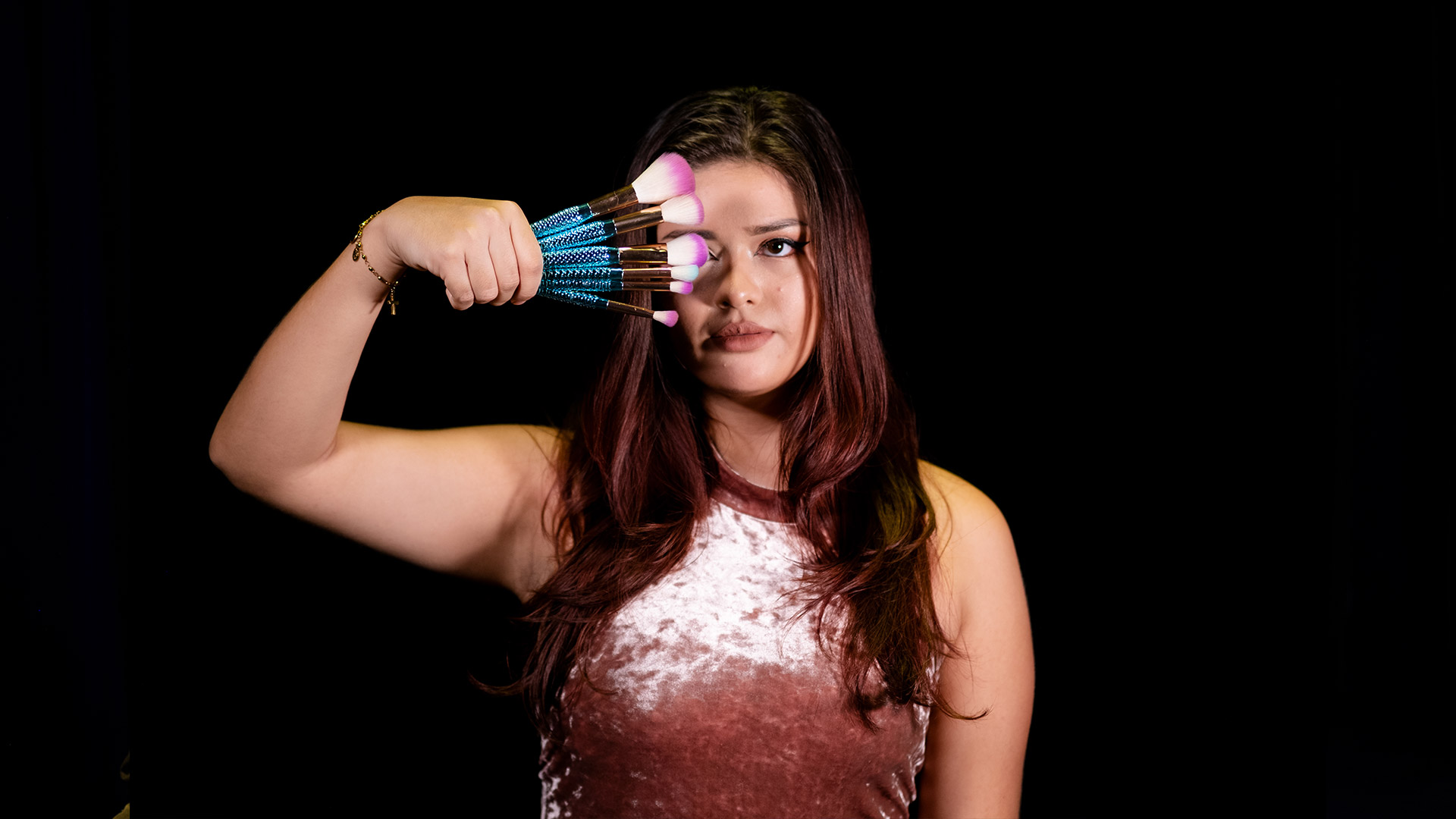 A photo of a young woman holding makeup brushes.