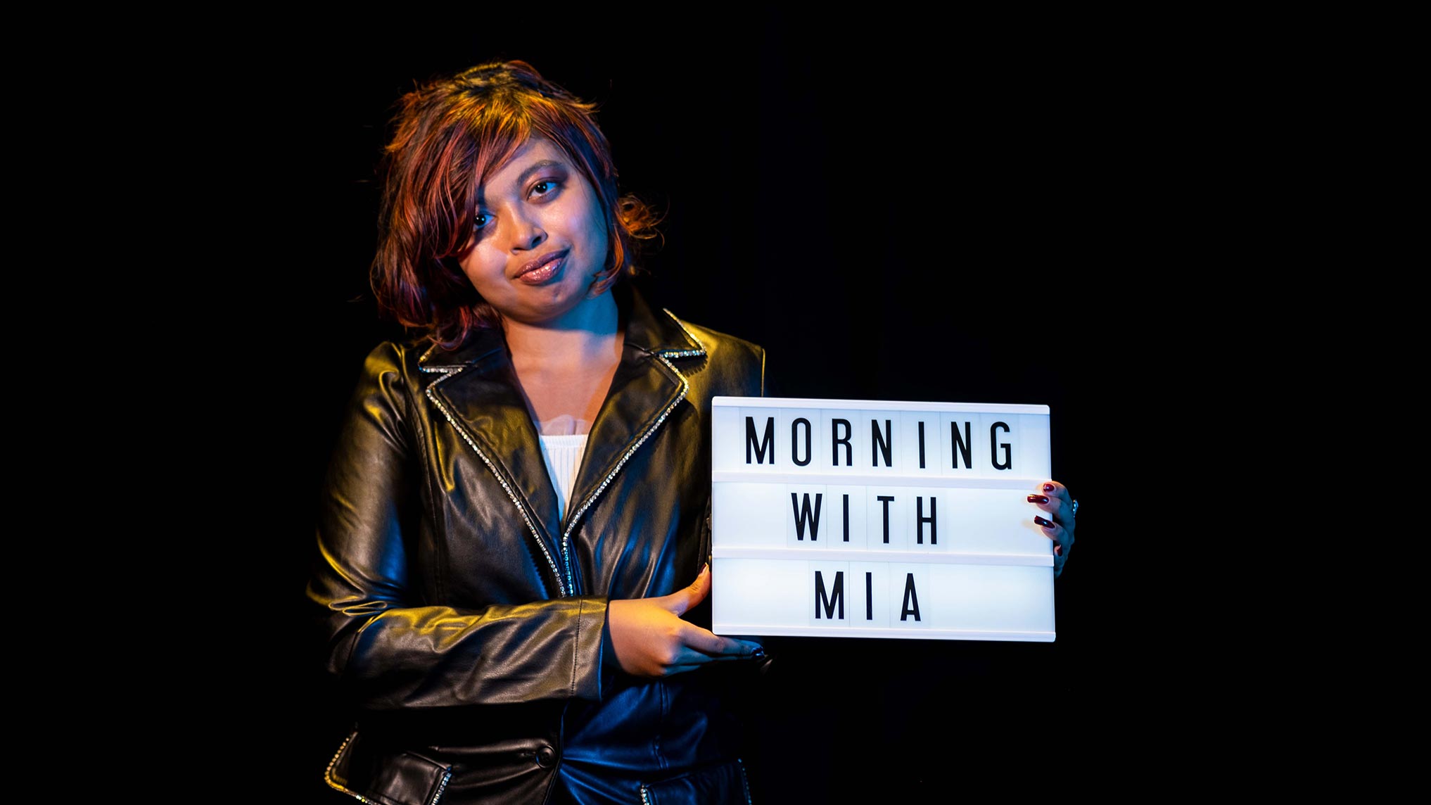 A photo of a young woman holding a sign that reads Morning With Mia