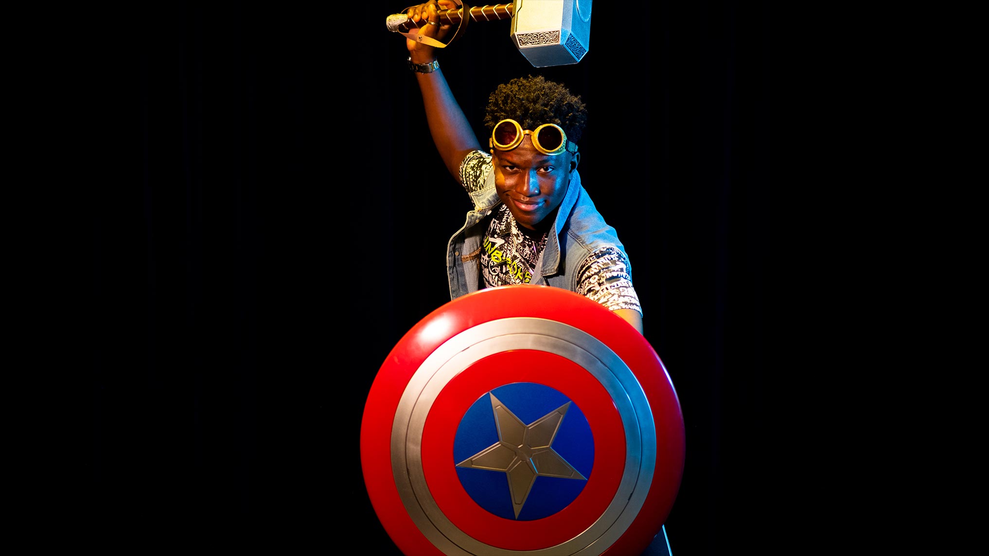 A photo of a young man with a captain America shield and Thor hammer.