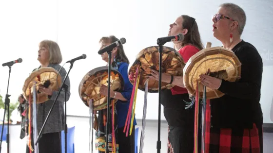 Four women playing musical instruments and singing into microphones.