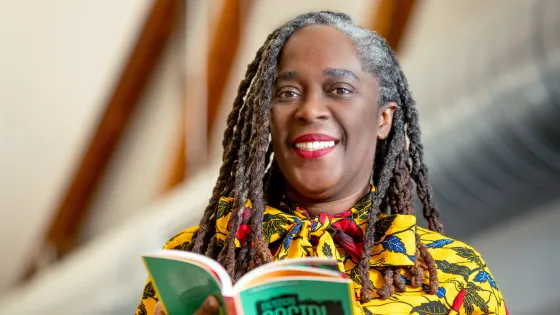 Photograph of Dr. Noel smiling into the camera while holding a book with a green cover in her hands. 
