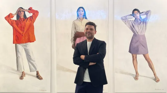 A man standing in front of three large paintings of stylish women.  