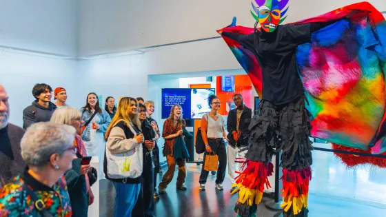 Person on stilts in colourful clothing performing in front of a small group