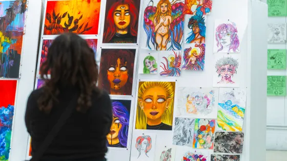 Person standing at a gallery wall covered in small paintings