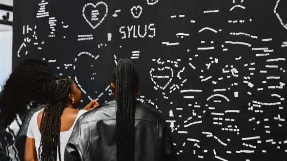 Three women with long braids interacting with a poetry wall