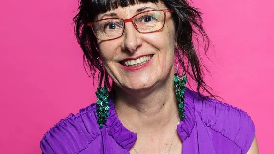 A woman with brown hair, brown eyes wearing red eye glasses, green earrings, purple shirt 