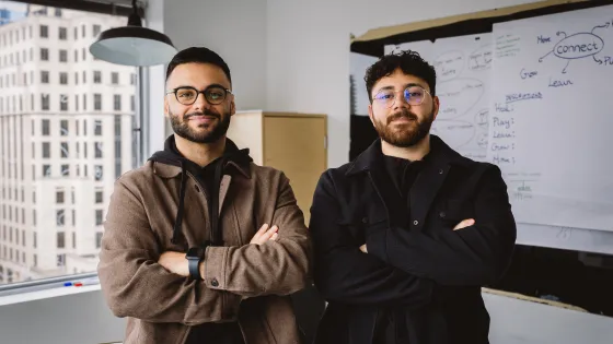 Award-winners Arian Shariaty (left) and Eli Saghbini (right) standing together in a meeting room. 