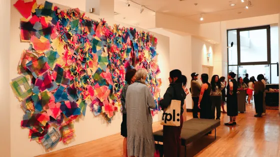 Group of people gathering at TO Live gallery with artwork by Laiken Breau displayed on the wall.