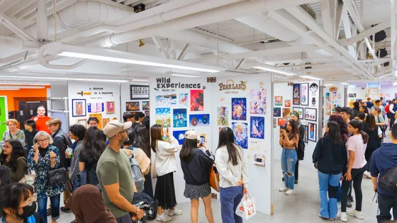 A crowd of people looking at displayed artworks set against white display walls. 