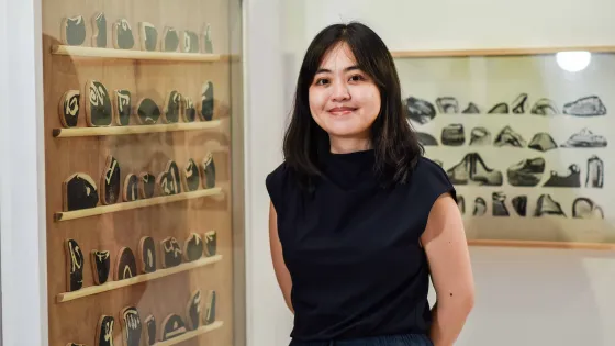 Photo of woman with dark hair, dressed in black, smiling in front of her artwork