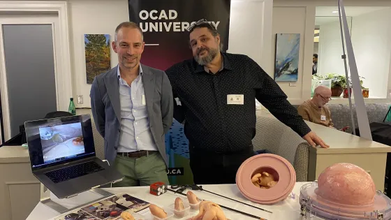 Dr. Tim Van Mieghem and Professor Francis LeBouthillier, standing in front of a table displaying medical surgical models, with an OCAD U banner in the background. 