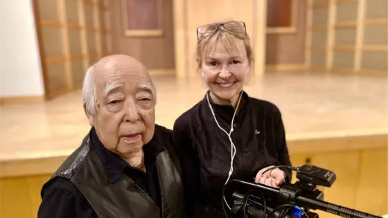 Japanese-Canadian man at left with a woman with blond hair and glasses on her head, holding a camera.