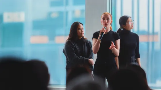 3 people speaking in front of a seated crowd