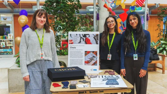Students standing next to display table of their product design. 