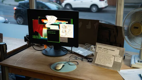 A work desk with a monitor sitting in front of a street facing window.
