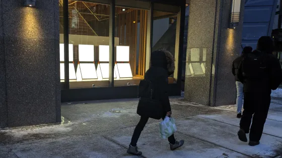 People walking on sidewalk beside light installation in window.